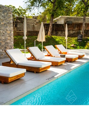 A poolside area with lounge chairs and umbrellas, a stone wall, and a signboard. - Zonte Terrace - 2BR Designer Loft with Surf Views (El Zonte)
