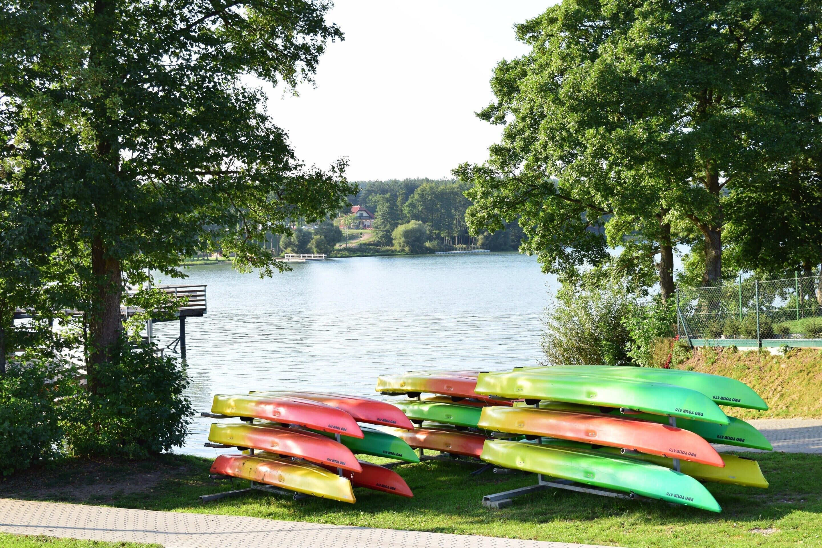 A row of canoes by a lake with a bench and trees in the background.