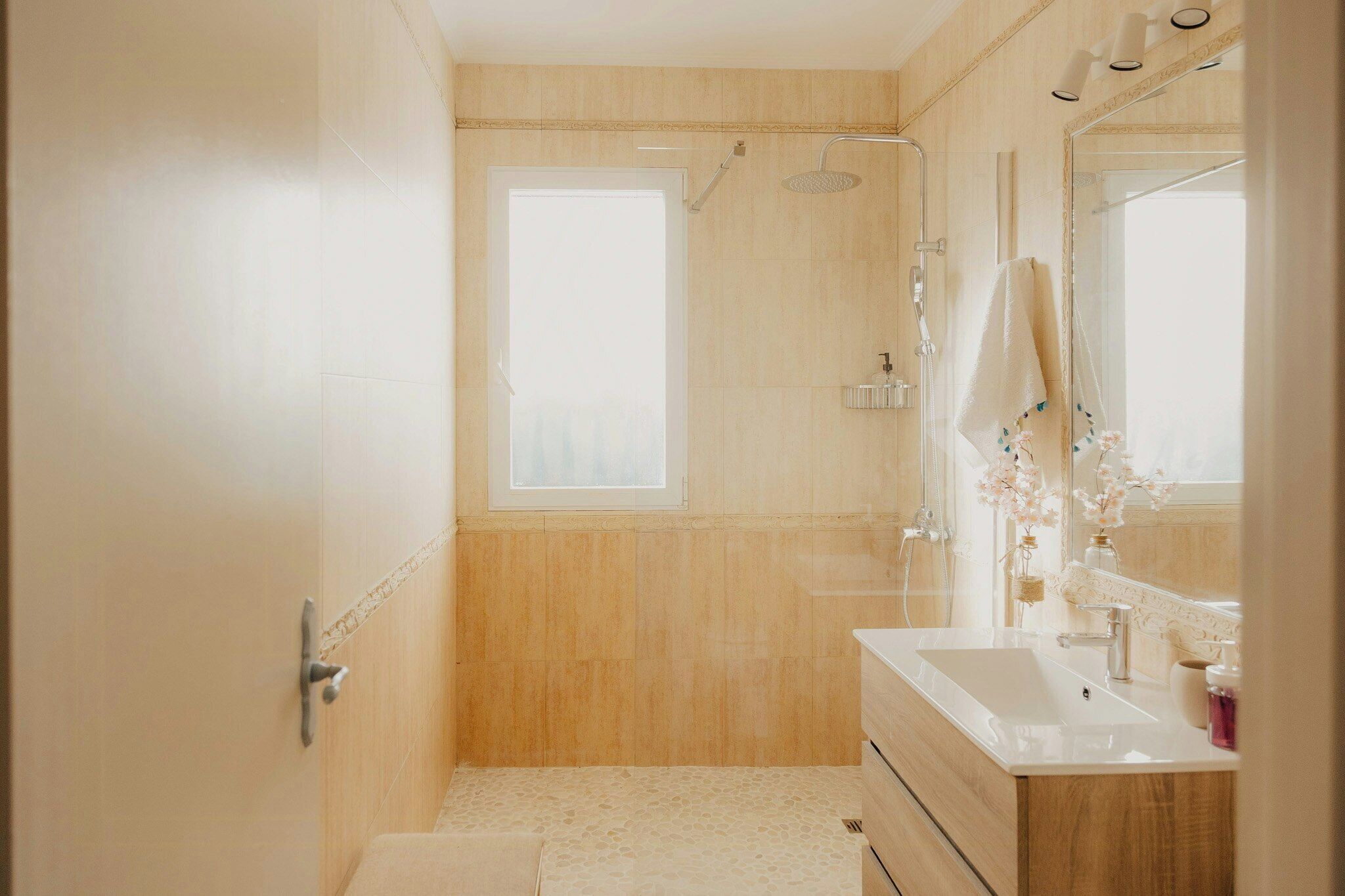 A bathroom with a shower, a sink, a mirror, and a window.