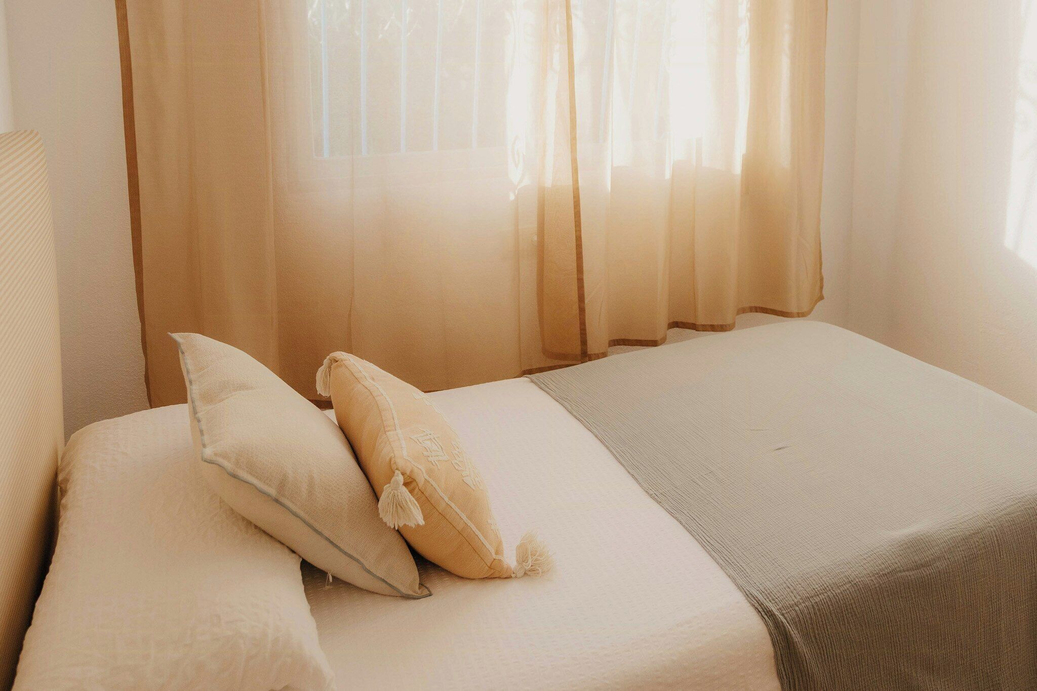 A bed with two pillows, a blanket, and sheer curtains.