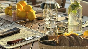 Ein Holztisch, gedeckt für eine Mahlzeit, mit einem Brotkorb, Zitronen, einer mit Minze gefüllten Wasserflasche und einem Glasbehälter.