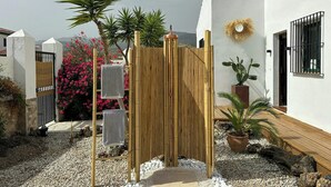 Ein Garten mit Bambuszaun, weißer Mauer, einem Kübelkaktus und einem Metalltor.