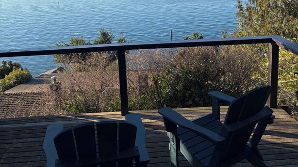 A deck with two Adirondack chairs and a picnic table overlooking a calm body of water.