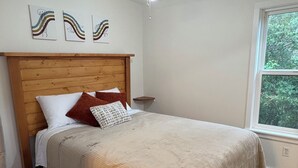 A bedroom with a wooden headboard, a bed with white and brown bedding, and a window with a view of greenery.