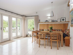 A dining area with a wooden table and chairs, a bench with cushions, a pendant light, and a view through large glass doors to an outdoor patio. - Lower Velwell Barn (Totnes)