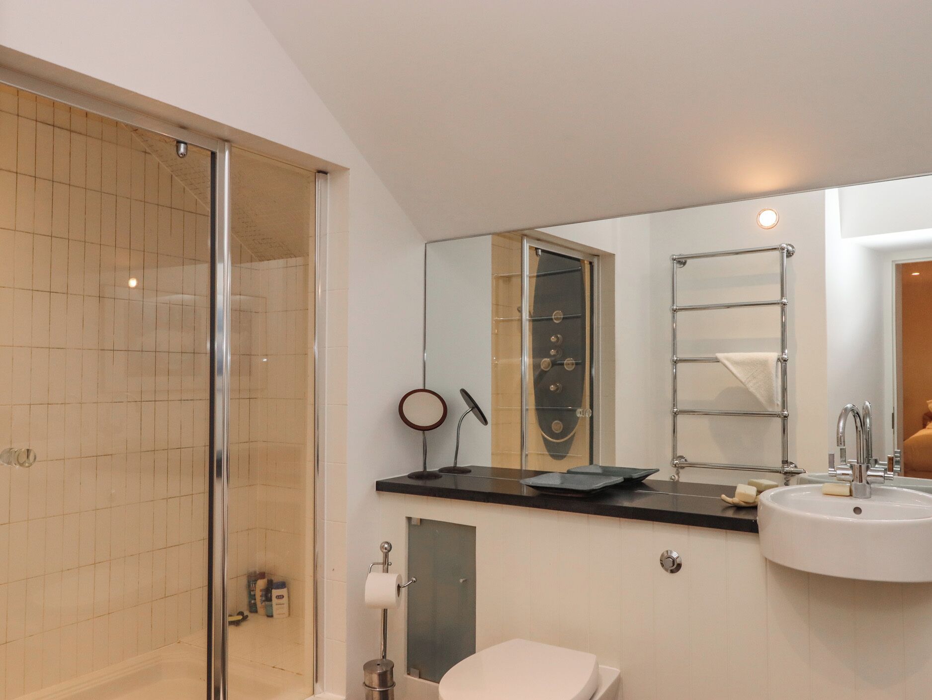Ein modernes Badezimmer mit Duschkabine aus Glas, großem Spiegel, weißem Waschbecken und Handtuchhalter.