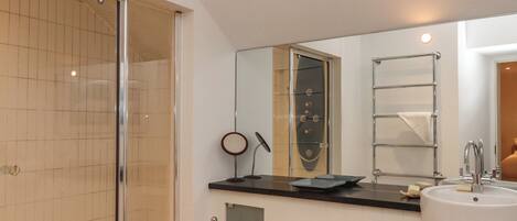 Ein modernes Badezimmer mit Duschkabine aus Glas, großem Spiegel, weißem Waschbecken und Handtuchhalter.