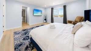 Habitación de hotel con cama, vista al mar por la ventana, una silla y una puerta que da a otra habitación.