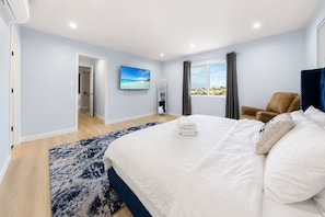 Quarto de hotel com cama, vista para o mar pela janela, uma cadeira e porta que dá para outro cômodo.