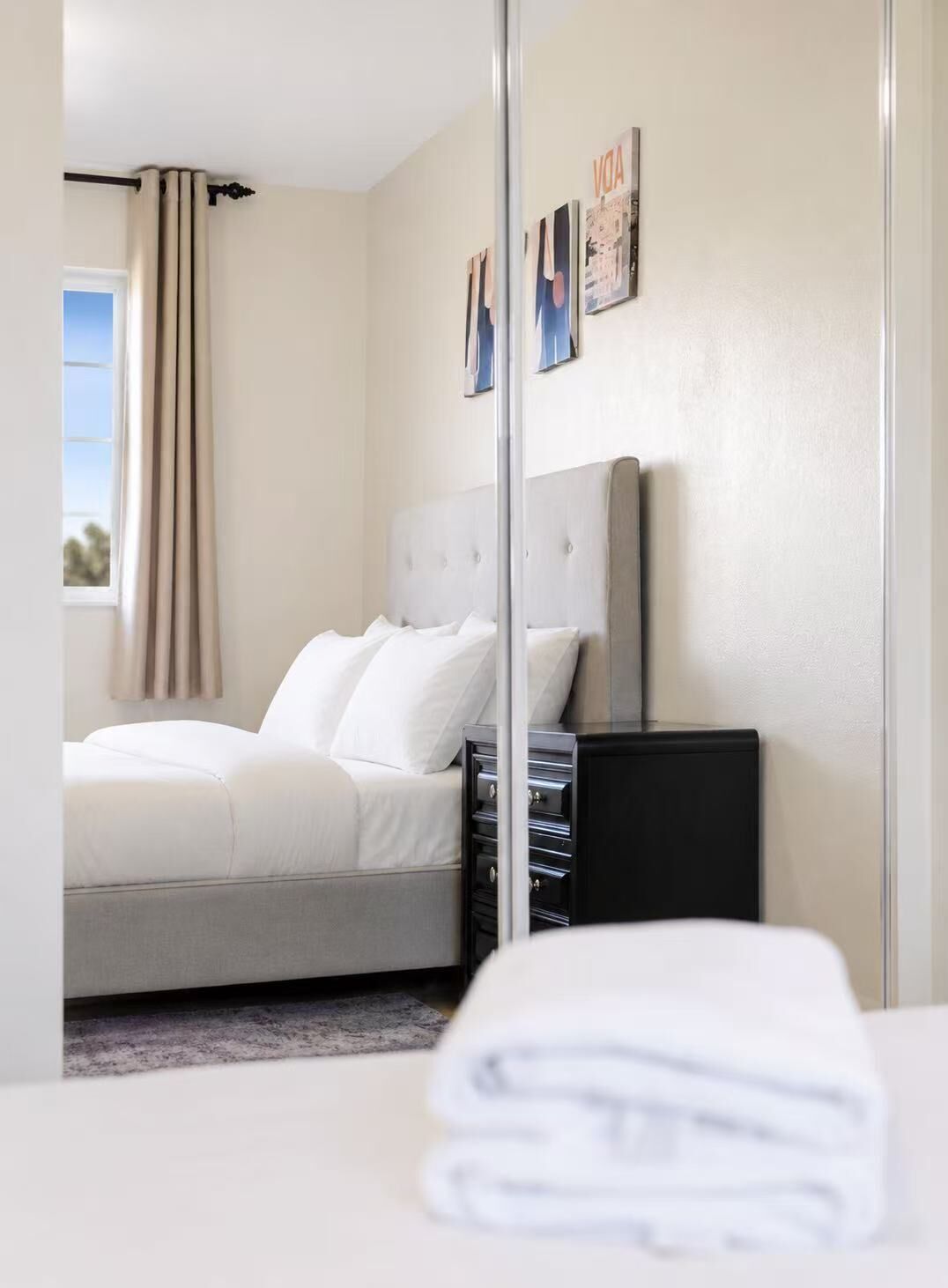 Une chambre d’hôtel avec un lit, une armoire, un miroir et une fenêtre avec des rideaux.