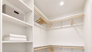 Un vestidor con estantes blancos, perchas de madera y suelo de madera.