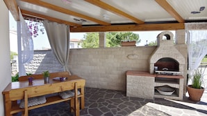 An outdoor patio with a stone floor, a wooden table with chairs, a stone oven, and a potted plant. - Modern Studio With Terrace (Umag)