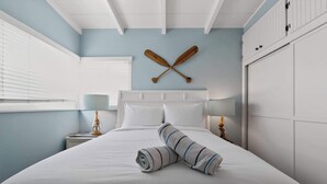 A neatly made bed with two rolled towels, a wooden paddle wall art, a bedside lamp, and a wardrobe. - Blue Heron Perch - 5 minute walk to beach, garage (Newport Beach)