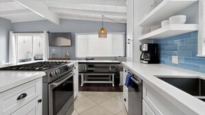 A modern kitchen with white cabinetry, a gas stove, a built-in oven, a coffee maker, and a blue-tiled backsplash. - Blue Heron Perch - 5 minute walk to beach, garage (Newport Beach)