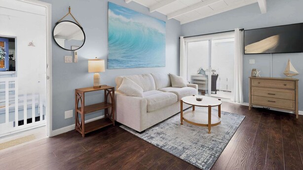 A living room with a sofa, a round coffee table, a mirror, and a painting of a wave. - Blue Heron Perch - 5 minute walk to beach, garage (Newport Beach)