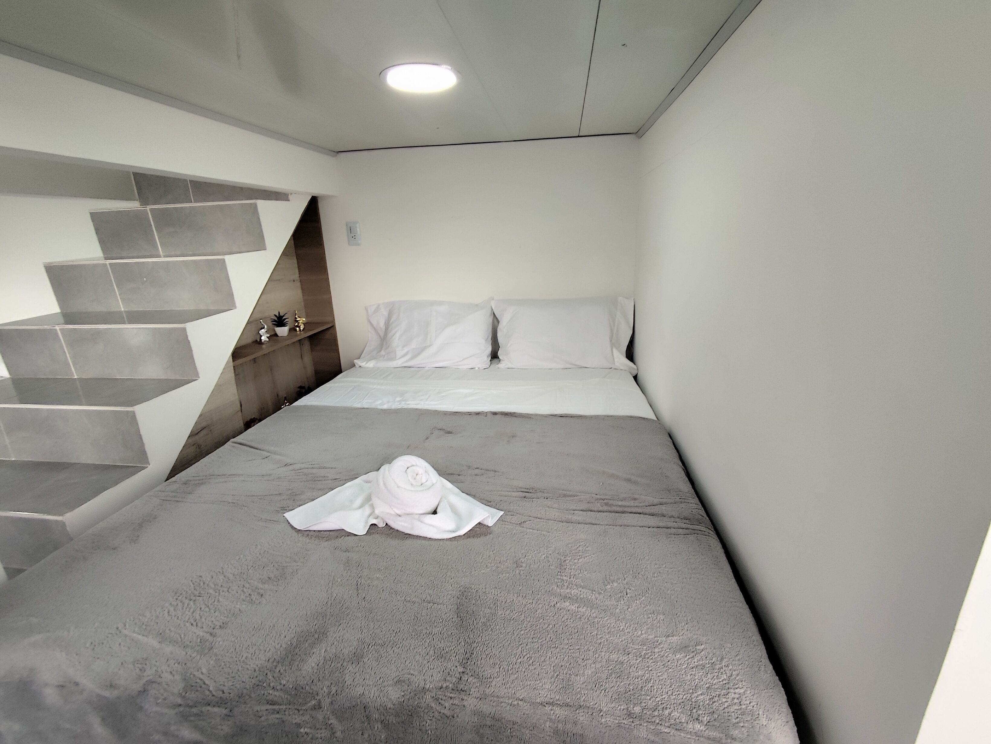 A modern hotel room with a bed, a neatly folded towel, and a staircase with a unique design.