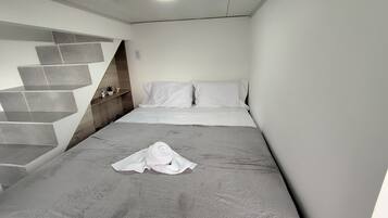 A modern hotel room with a bed, a neatly folded towel, and a staircase with a unique design.