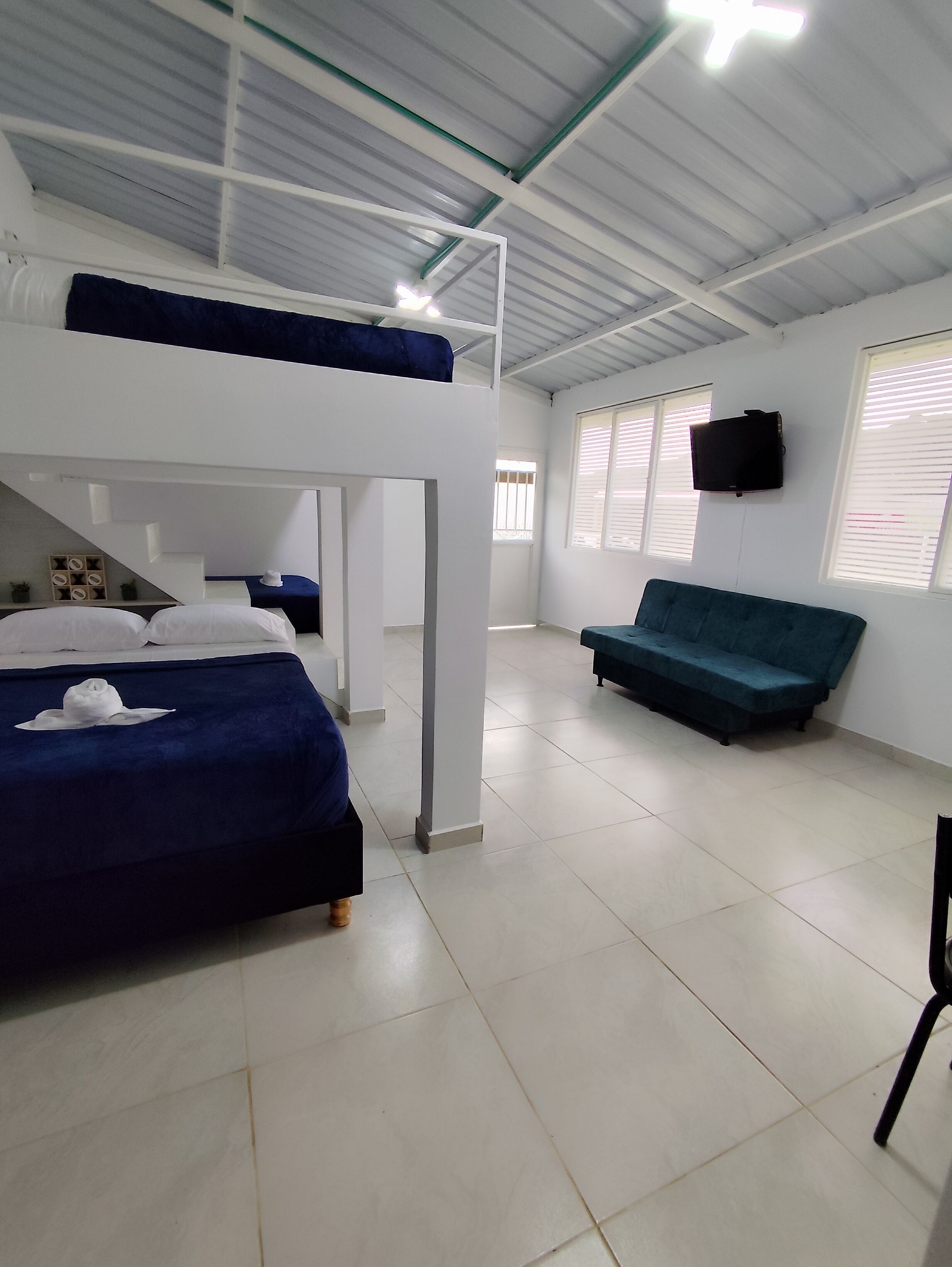 Una habitación con literas, un sofá, un televisor y suelo de baldosas.