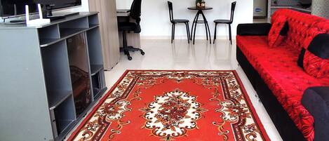 Una sala de estar moderna con un televisor de pantalla plana, un sofá rojo, una mesa de centro y una alfombra estampada.