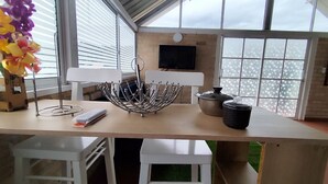 A modern kitchen with a large window, a metal kitchen island, white bar stools, and a flat-screen TV mounted on the wall. - Cantabria Hospedaje (Popayán)
