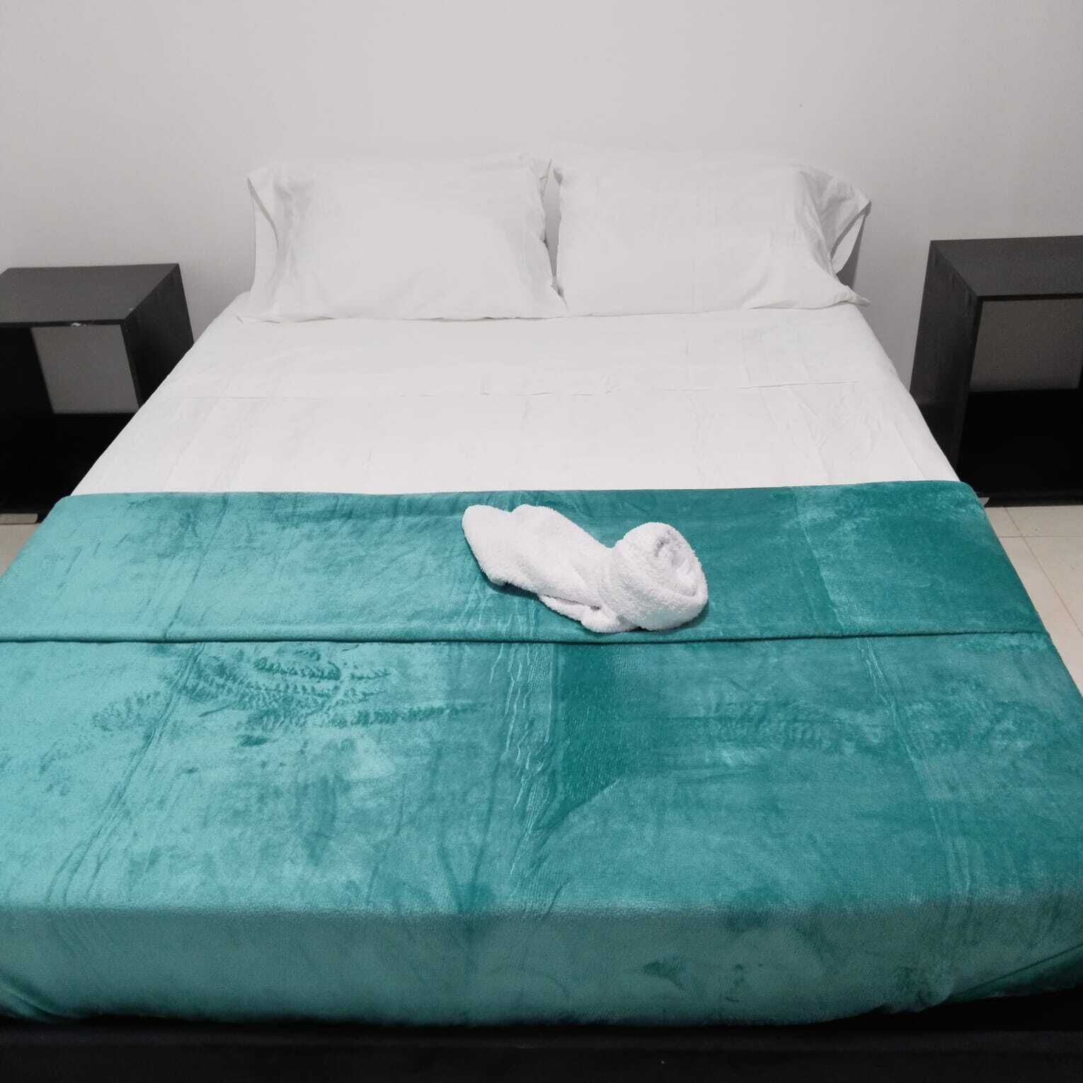 Una cama con una colcha color turquesa y una toalla blanca encima.