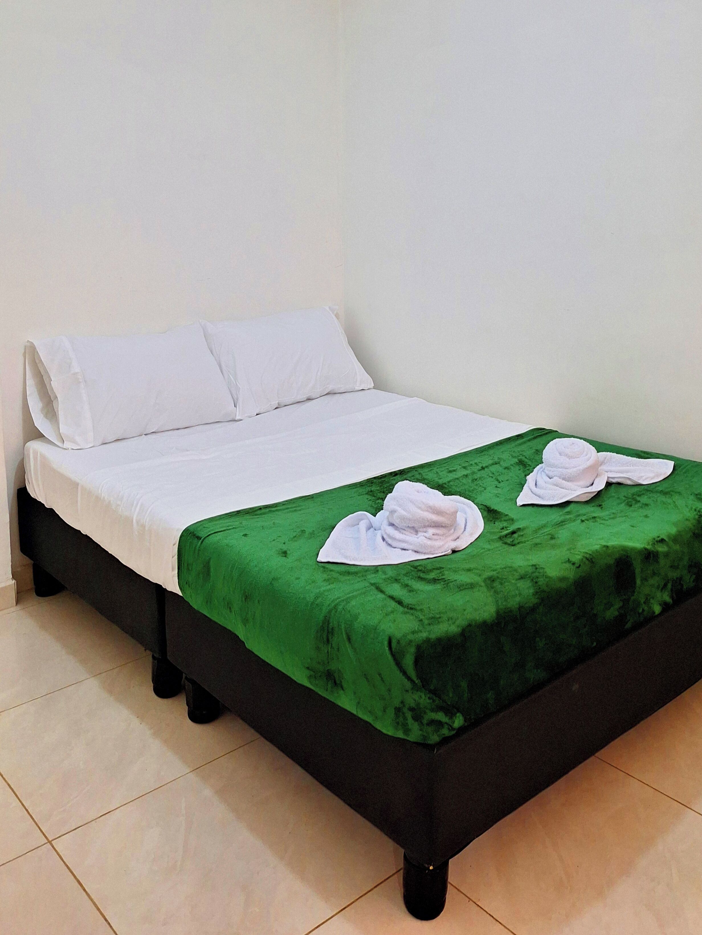 A single bed with white linens, a green bedspread, and two white towels on the footboard.