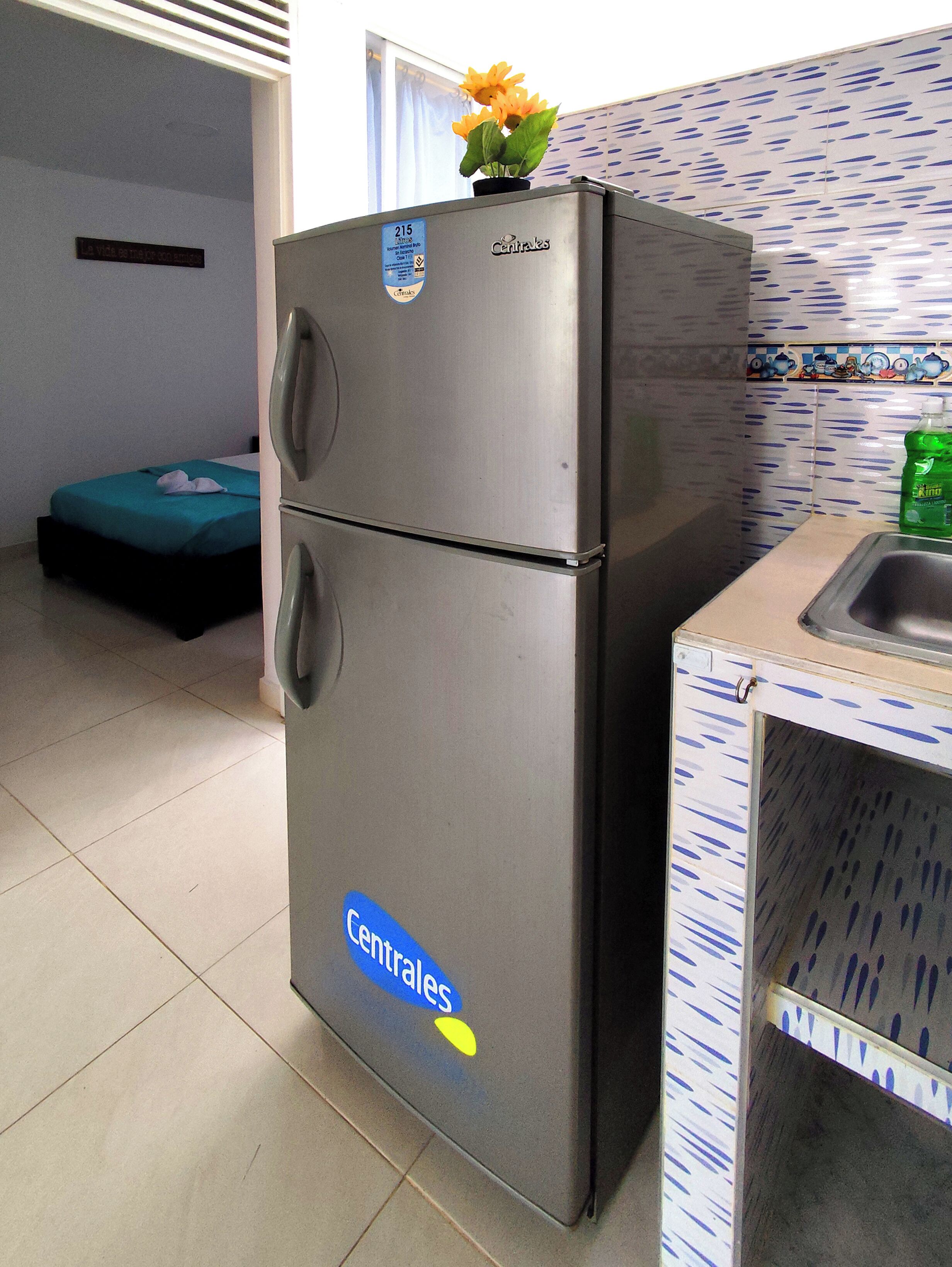Una cocina con refrigerador, lavamanos y ventana con cortinas.