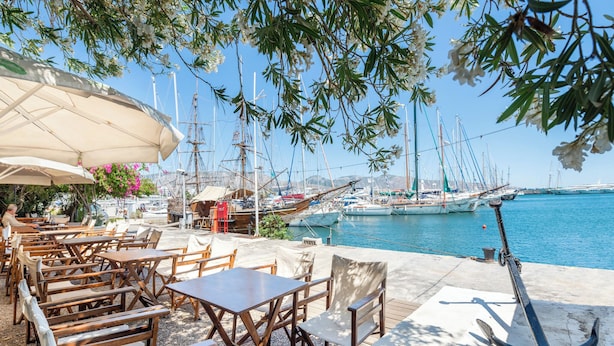 Een café aan zee met terras, uitzicht op de jachthaven en een groot anker op het dek.