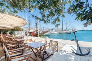 A seaside café with outdoor seating, a view of the marina, and a large anchor on the deck. - Athenian Riviera Suite ~Ano Voula (Athens)