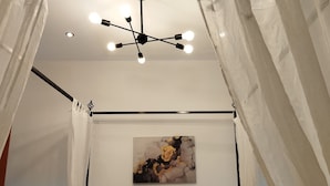Een kamer met een plafondlamp, een schilderij aan de muur en doorschijnende gordijnen.