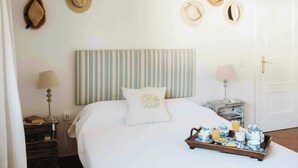 A neatly made bed with striped headboard, a bedside table with a lamp, and a tray of breakfast items. - Centuries-old olive finca with pool in Cádiz (Barbate)