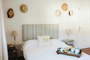Un lit bien fait, avec une tête de lit à rayures, une table de chevet avec une lampe et un plateau contenant des articles pour le petit-déjeuner.