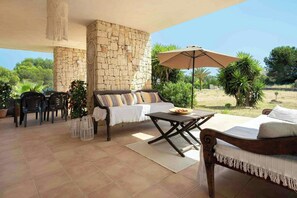 Eine überdachte Terrasse mit Steinmauer, einer Couch, einem Tisch und Stühlen.