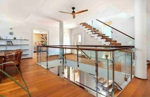 Ein modernes Interieur mit Glasgeländer, einer Holztreppe und einem Deckenventilator.