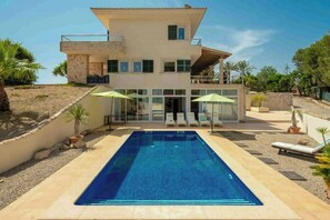 Ein modernes, zweistöckiges Haus mit Schwimmbad, Sitzgelegenheit im Freien und einer Steinschmalseite.