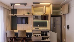 Een compacte keuken met inbouwapparatuur, een eethoek met stoelen, en een aan de muur bevestigde televisie.