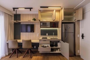 A compact kitchen with built-in appliances, a dining area with chairs, and a TV mounted on the wall. - Studio Completo a 5min do Nubank Parque | GP128 (Perdizes)