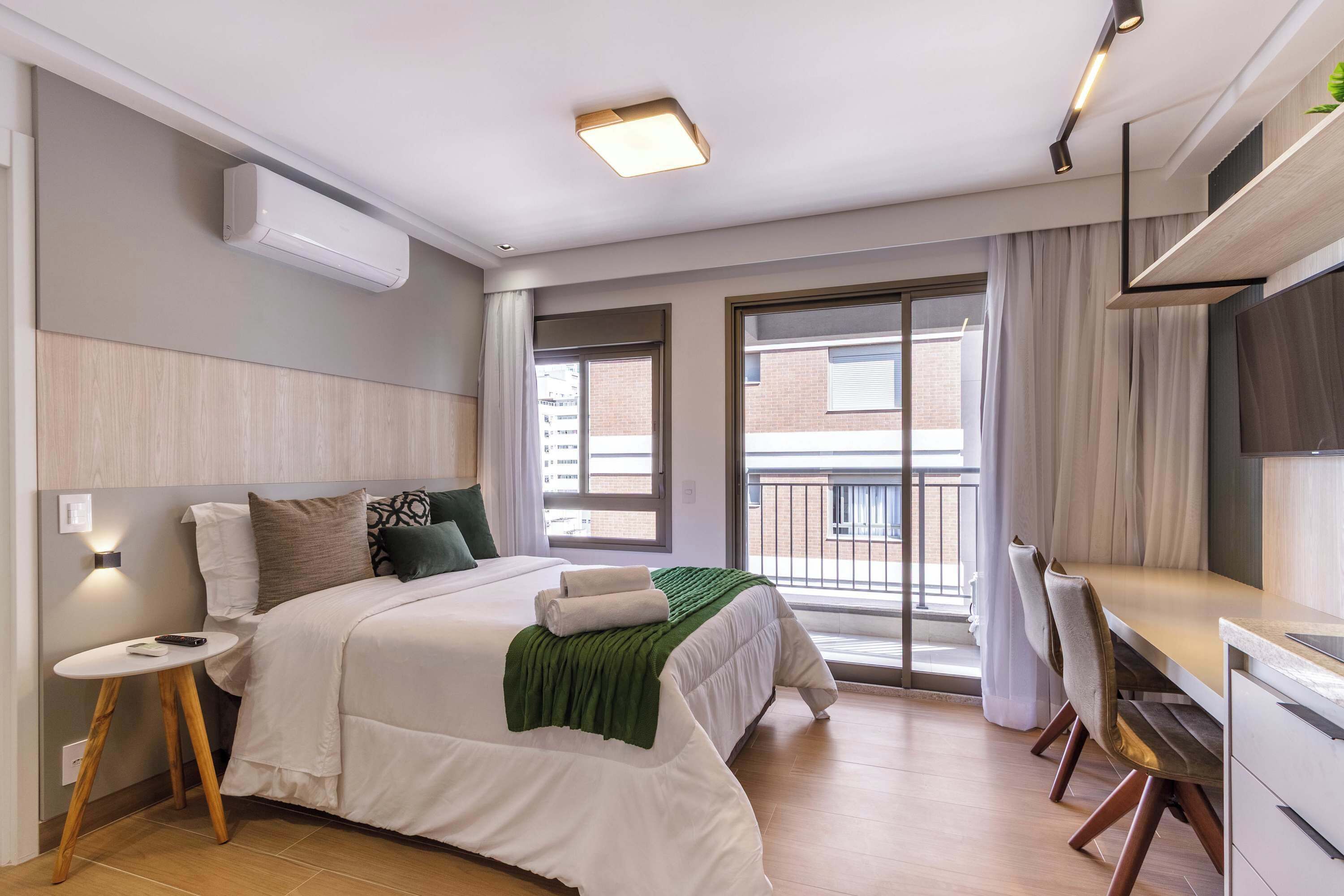 A modern hotel room with a bed, bedside table, and a balcony with a view.