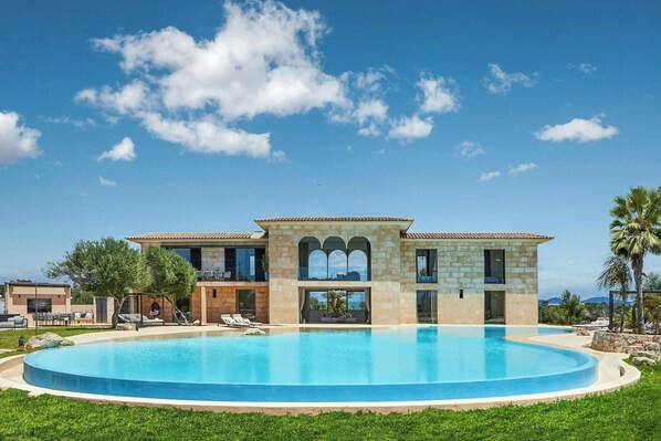 A two-story house with a swimming pool, stone facade, and a view of the mountains.