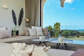 A modern living room with a sofa, two round tables, and a view of the sea.