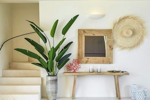 A staircase, a potted plant, a wall-mounted mirror, and a small table with candles and a book.
