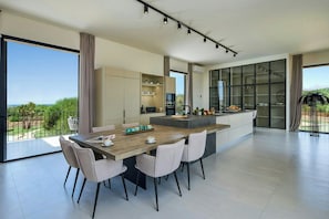 A modern kitchen with a dining area, large windows, and a view of greenery.