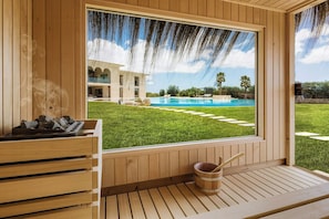 A wooden sauna with a view of a swimming pool and a building in the background.
