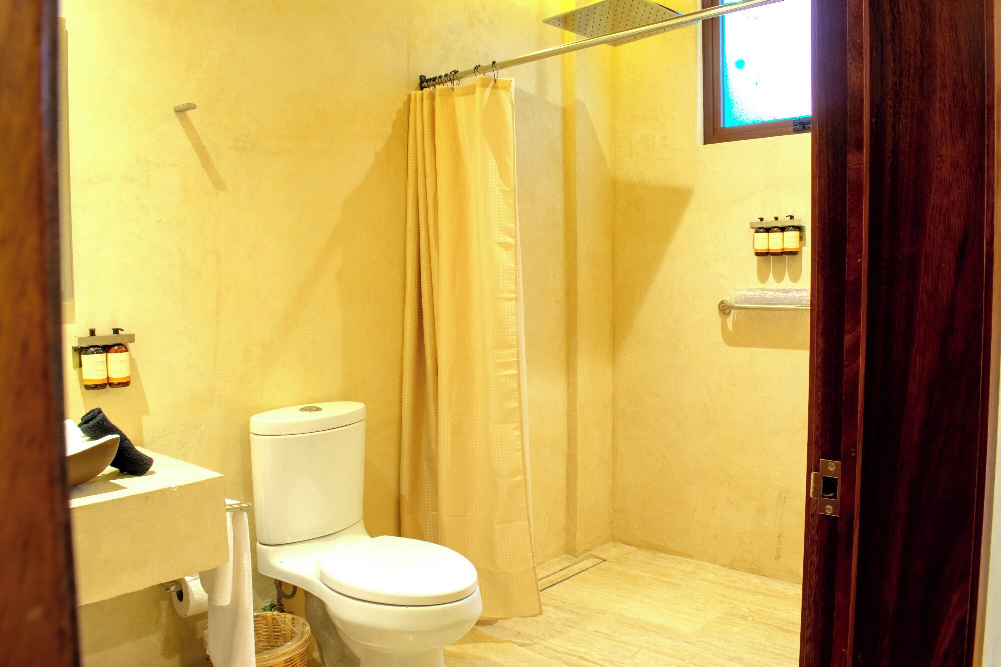 A small bathroom with a toilet, a shower curtain, a towel rack, and a wall-mounted soap dispenser.