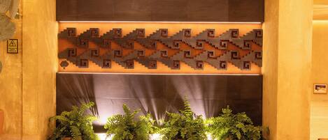A reception area with a patterned wall, a potted plant arrangement, and a caution sign.