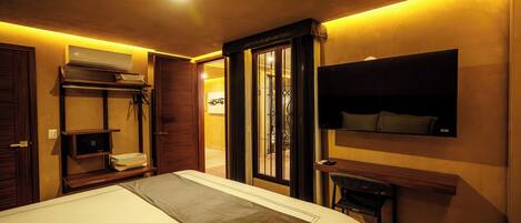 A hotel room with a bed, a desk, a TV, a wardrobe, and an air conditioning unit.