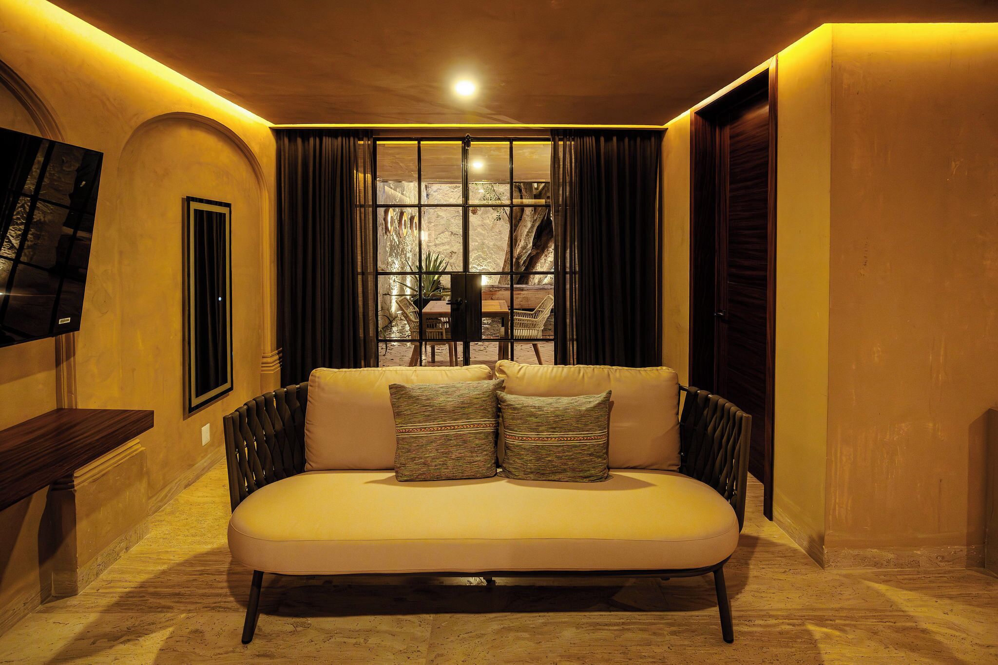 A sofa with cushions, a television mounted on the wall, and a window with curtains.