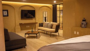 Ein Hotelzimmer mit einer Couch, einem kleinen Tisch, einem Bett und einem großen Fenster mit Vorhängen.
