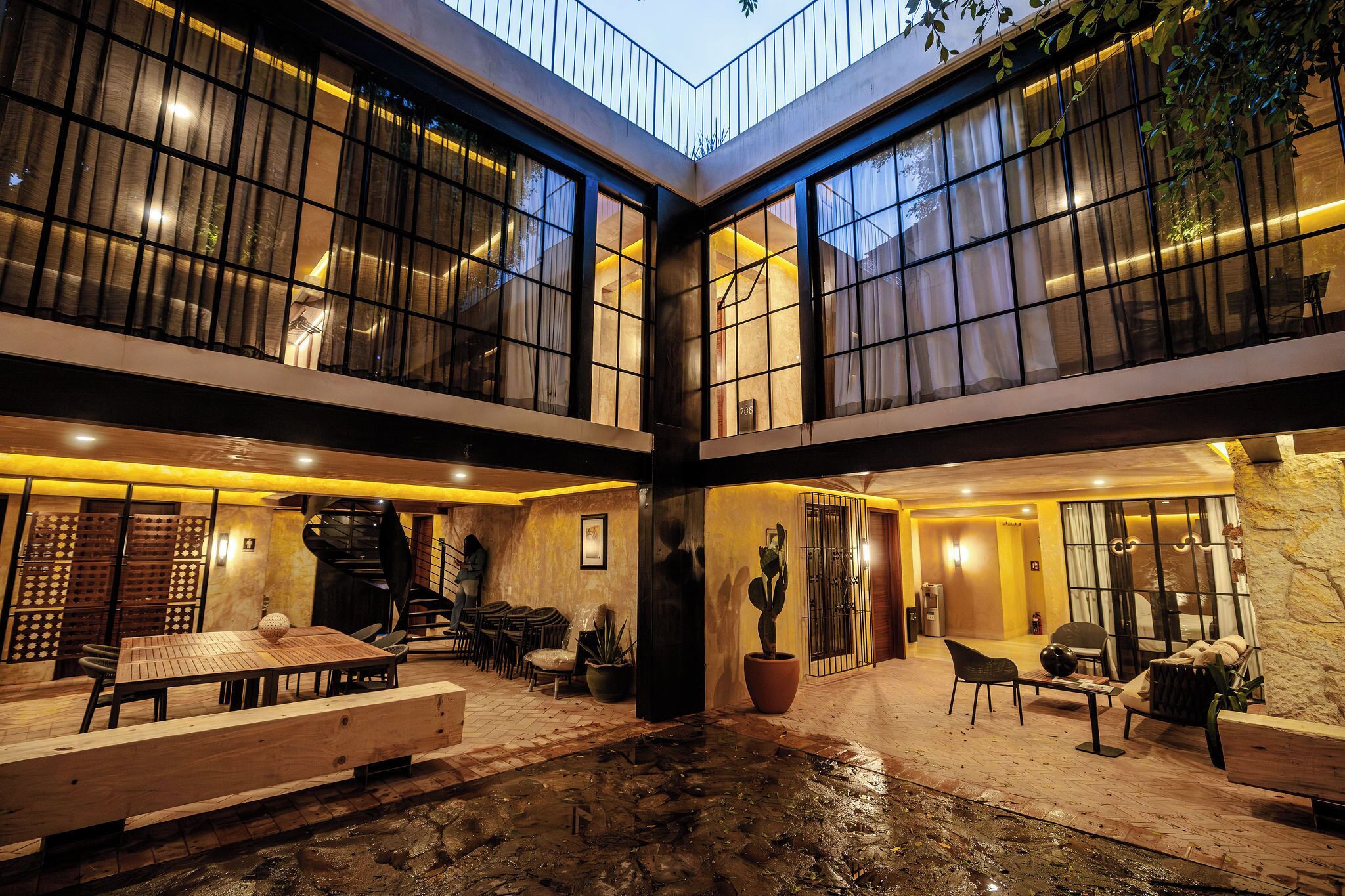 A spacious indoor courtyard with a wooden table and chairs, a potted plant, and a stone wall.