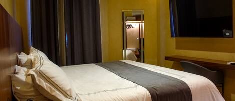 Habitación de hotel con cama, escritorio, silla, televisor y espejo.
